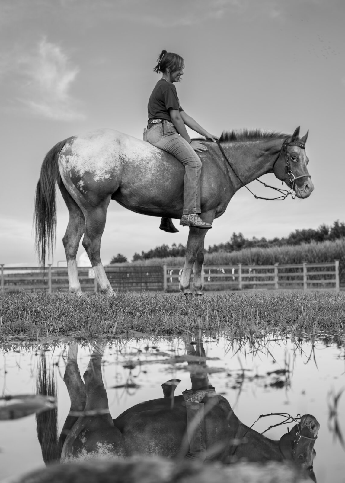 Black and white photograph of a rider and horse reflected in still water