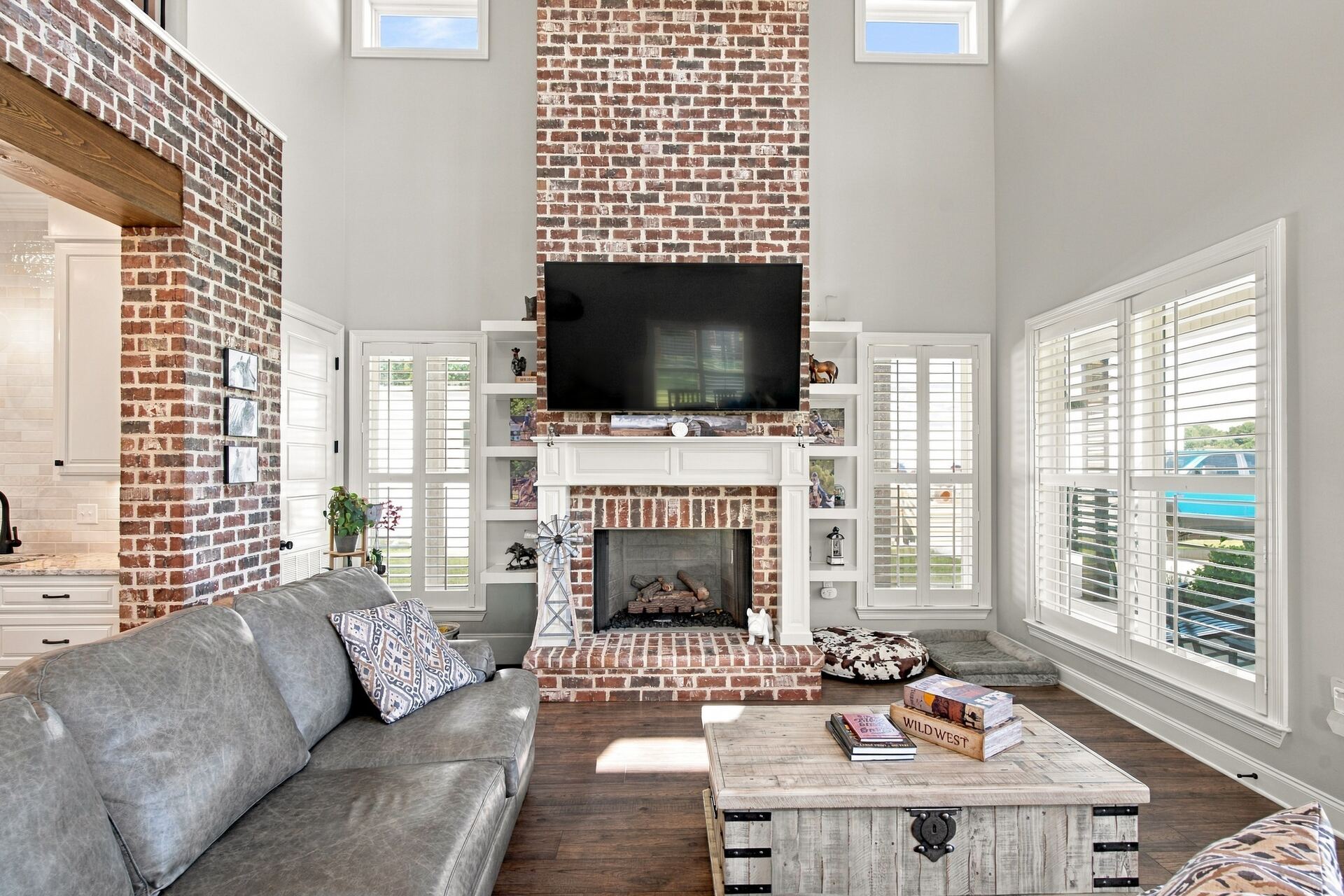 Living room with a brick fireplace, built-in shelving and plantation shutters